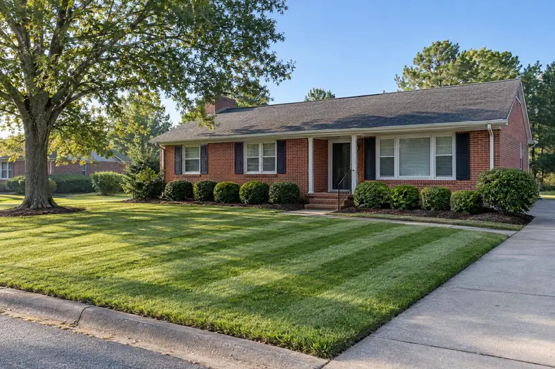 After: the same front yard mowed in clean stripes, edges cut sharp along the walk and curb, fresh dark mulch and shaped boxwoods